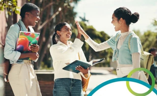 Three students outside a college, books under their arms, high-fiving after comparing notes.